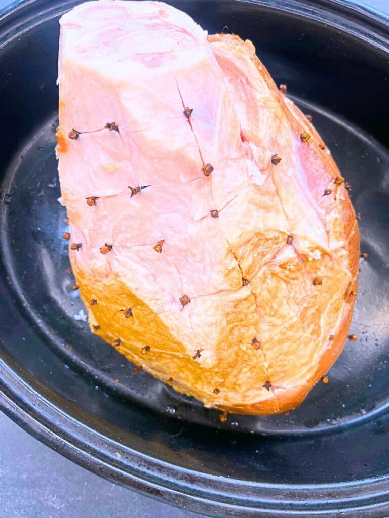 A ham shank that has diagonal cuts on the outside. There are whole cloves studded into the outside of the ham.