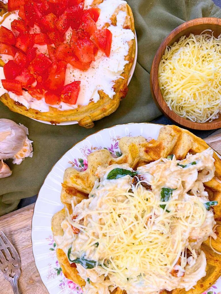 Two cheese waffles. One is spread with cream cheese and diced tomatoes. The other savoury waffle has a cheese chicken, tomato, and spinach mixture.