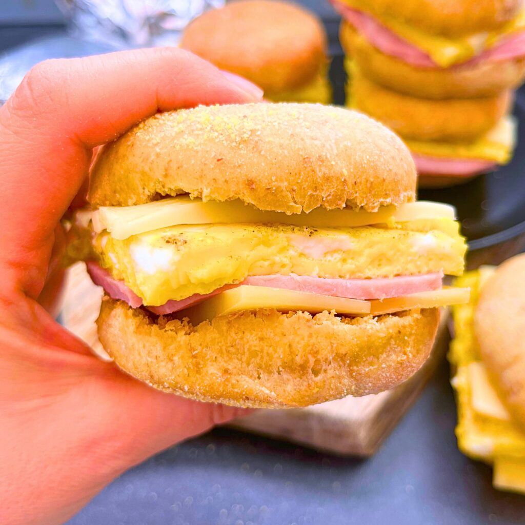 A woman is holding a breakfast sandwich filled with cheese, ham, and scrambled eggs.
