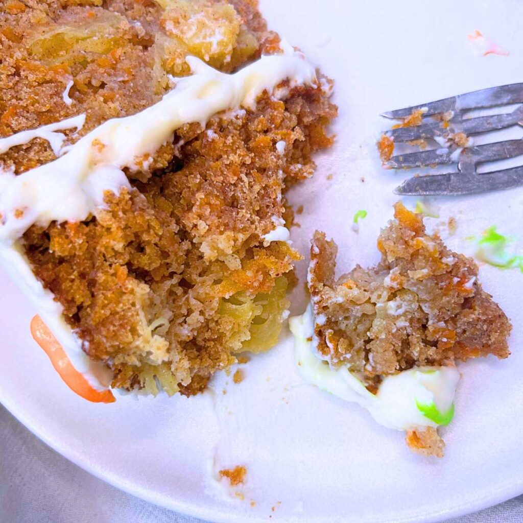 A slice of carrot cake on it's side. There is a bite-sized piece removed and a fork to the side.