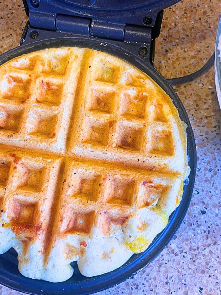 A cooked savoury sourdough cheese waffle on a waffle iron.