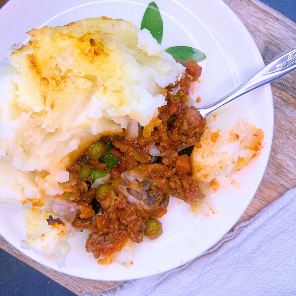 A white plate with a serving of shepherd's pie. There is a fork on the plate.