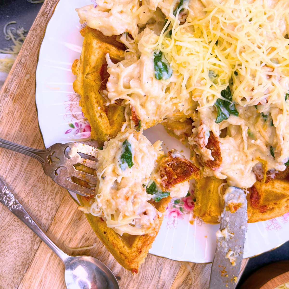 A fork is in a slice of a savoury waffle that has a chicken, cheese, tomato, and spinach mixture on top.