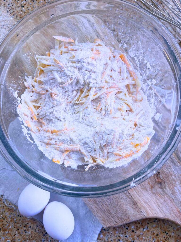 A glass bowl filled with flour and shredded cheese.