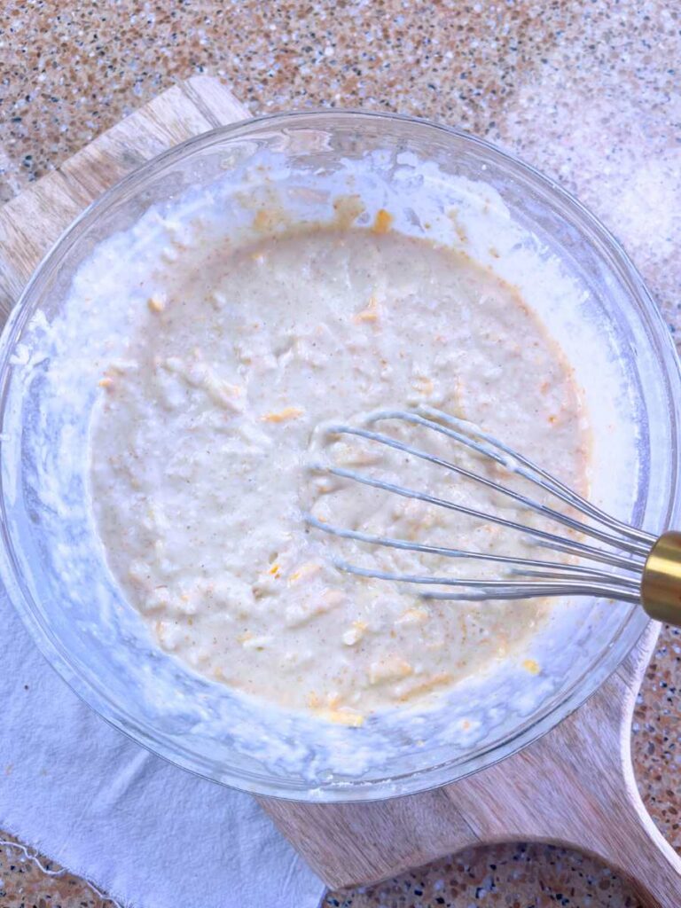 A glass bowl filled with savoury sourdough cheese waffle batter.