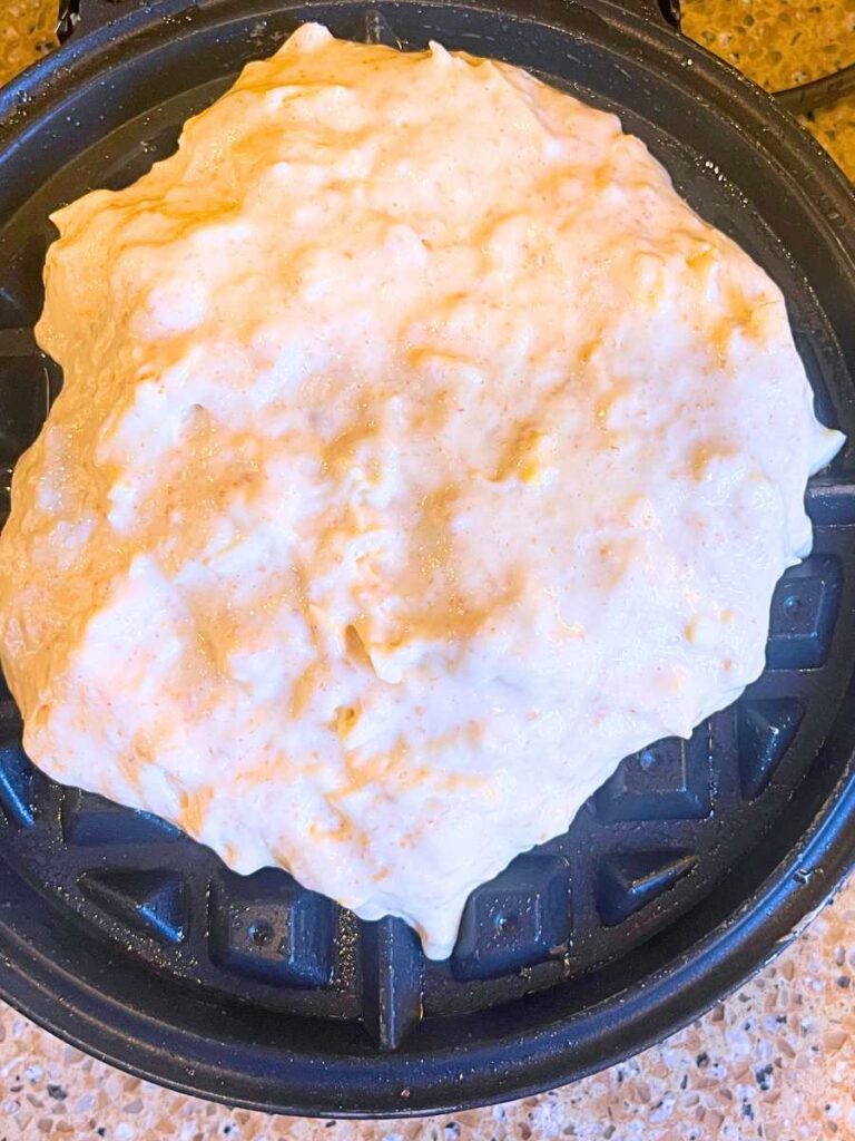 A waffle iron with savoury sourdough cheese waffle batter inside.