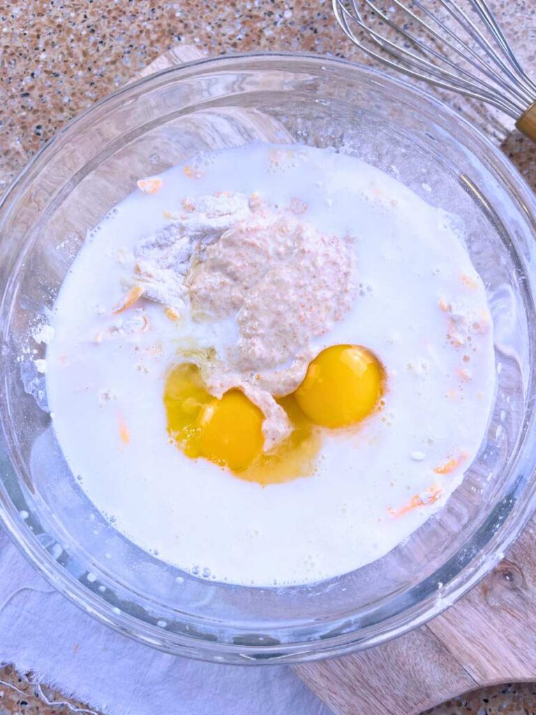 A glass bowl filled with milk, sourdough discard, and eggs.