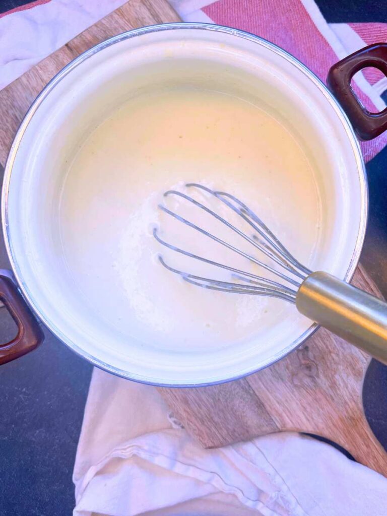 A white sauce pot with a béchamel sauce and a whisk.