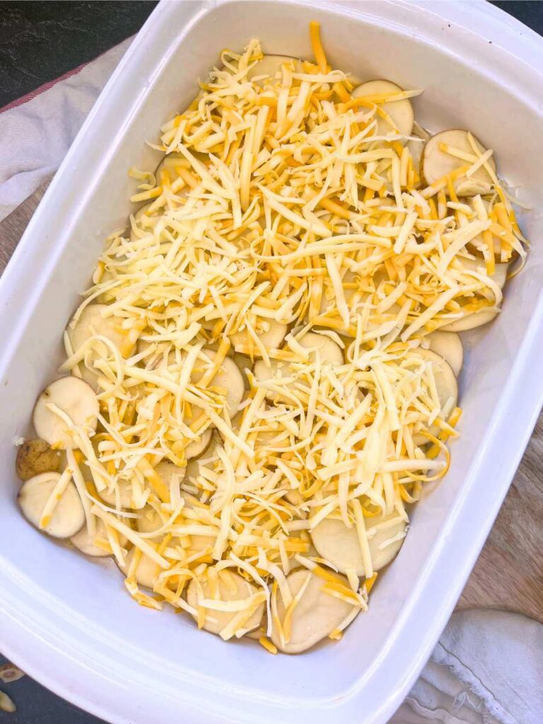 A white casserole dish with a layer of sliced potatoes and grated cheese.
