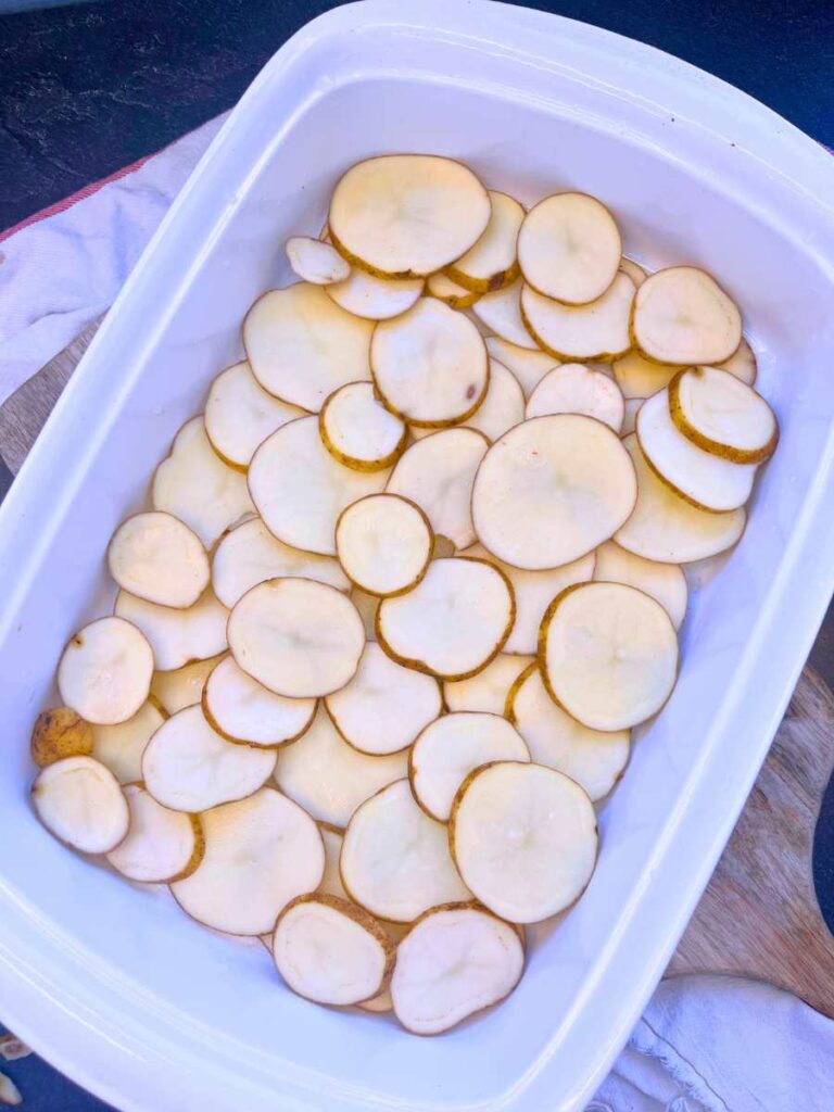 A white casserole dish with a layer of sliced potatoes in the bottom.