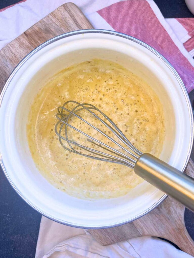 A white sauce pot with a roux and a whisk.