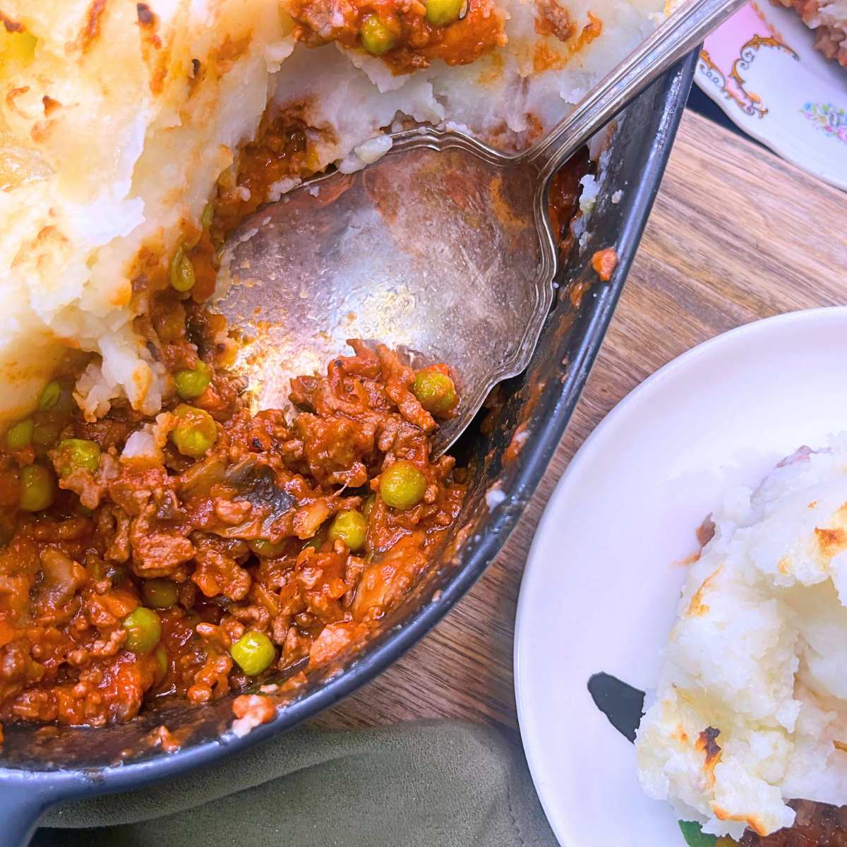An overhead view of a shepherd's pie casserole with a serving spoon inside. There is a serving on a white plate off to the side.