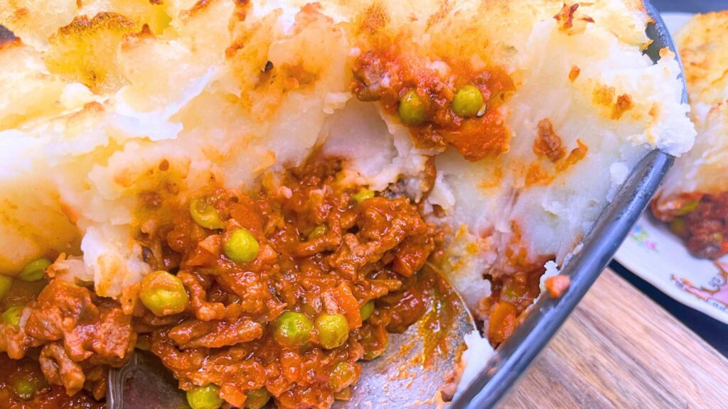 A shepherd's pie in a black casserole dish. There are some servings removed.