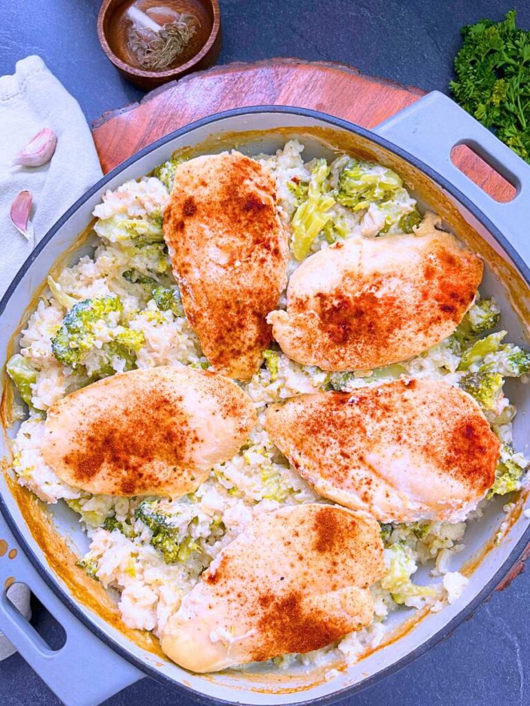 A baked rice and broccoli casserole with cooked chicken breast on top. There is paprika garnishing the top of the casserole.