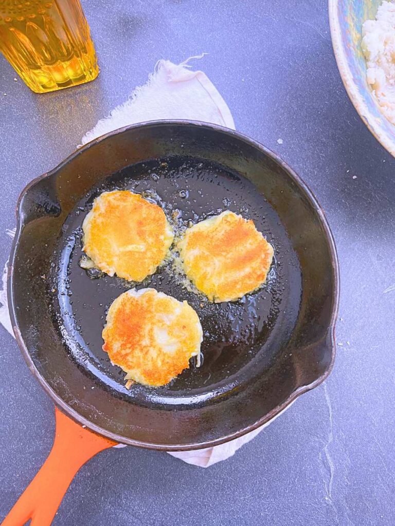 Three fried potato pancakes in a black and orange frying pan.