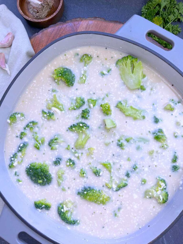Chopped broccoli in a cream sauce inside of a grey Dutch oven.