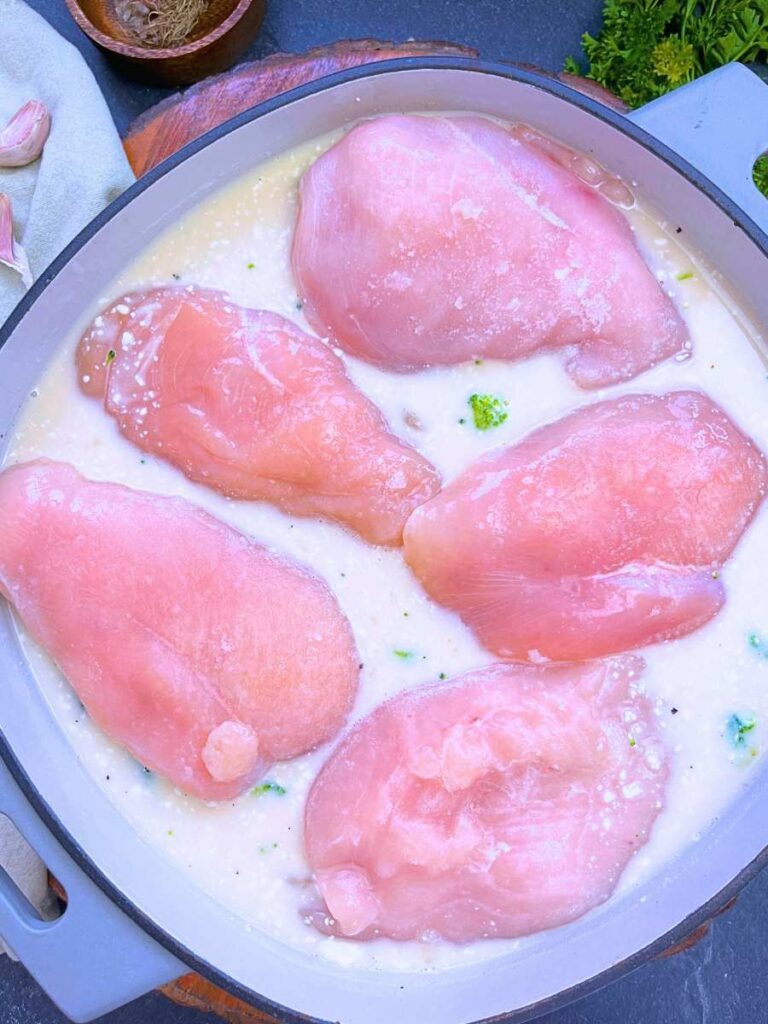 Broccoli in a cream sauce with raw chicken breast on top.