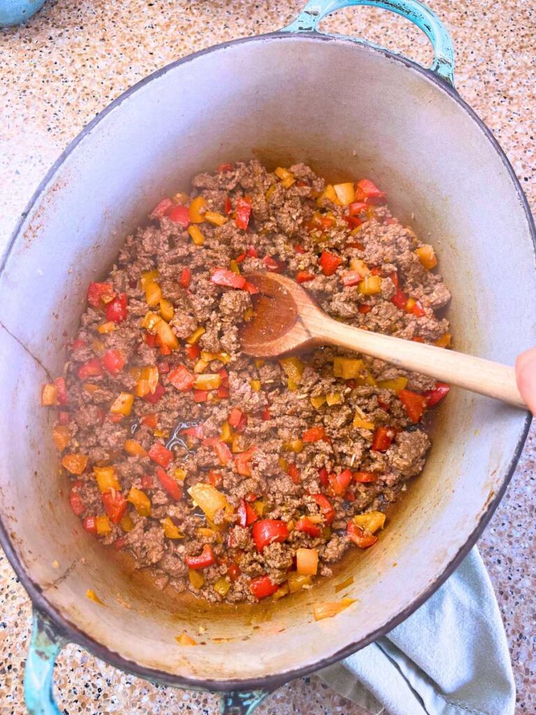 A Dutch oven with cooked peppers and ground beef.