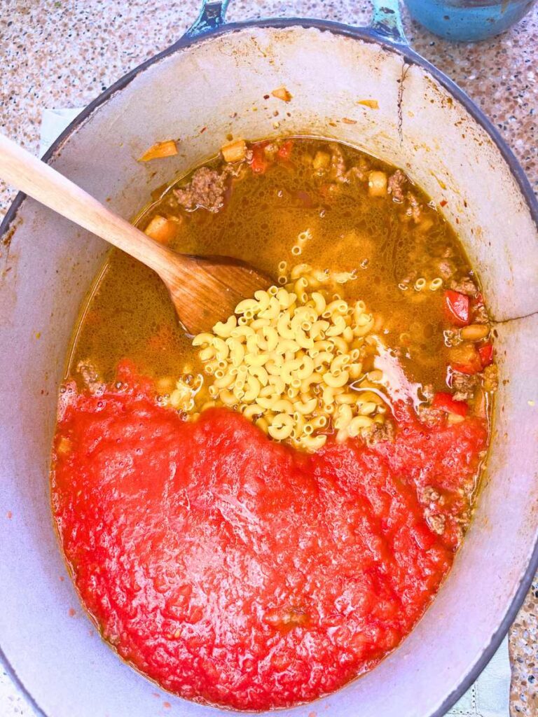 A large Dutch oven with cooked ground beef macaroni and tomato sauce inside.