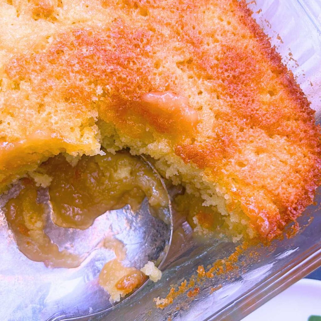 A baked pouding chômeur with slices removed. There is a large serving spoon inside the dish.