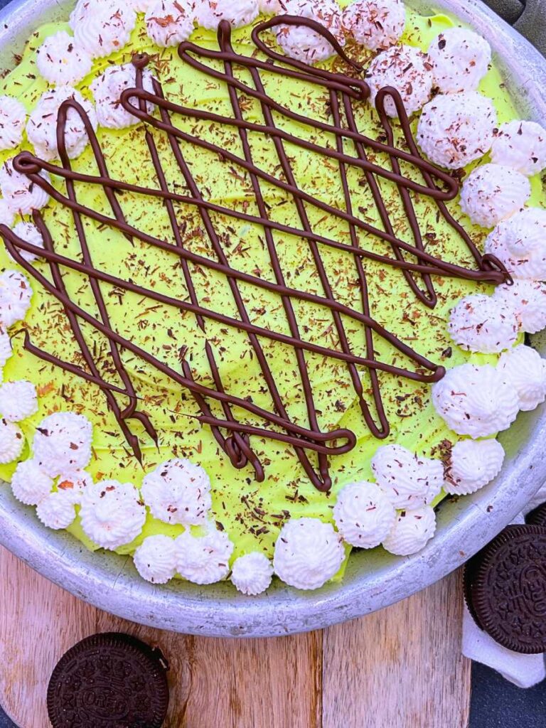 An overhead view of a full grasshopper pie with mint chocolate drizzle and whipped cream on top.