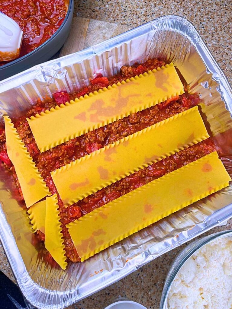An aluminum casserole pan with meat and tomato sauce and lasagna noodles on top.