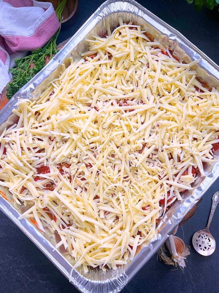 A frozen lasagna in an aluminum pan with grated mozzarella cheese on top.