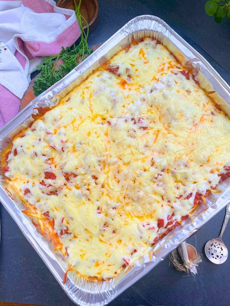 A partially baked freezer lasagna in an aluminum pan with melted mozzarella cheese on top.