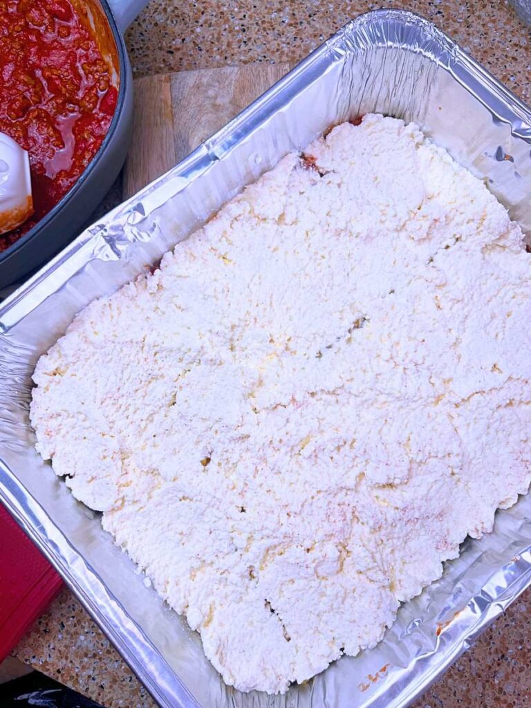 An aluminum rectangular pan with a lasagna layer of ricotta cheese.