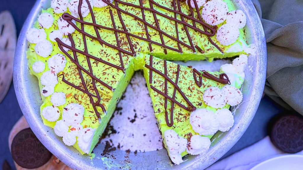 A grasshopper pie that has been sliced. It is decorated with mint chocolate drizzle and whipped cream.