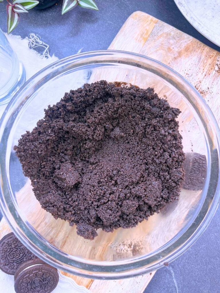 Chocolate cookie crumbs and melted butter mixed in a glass bowl.