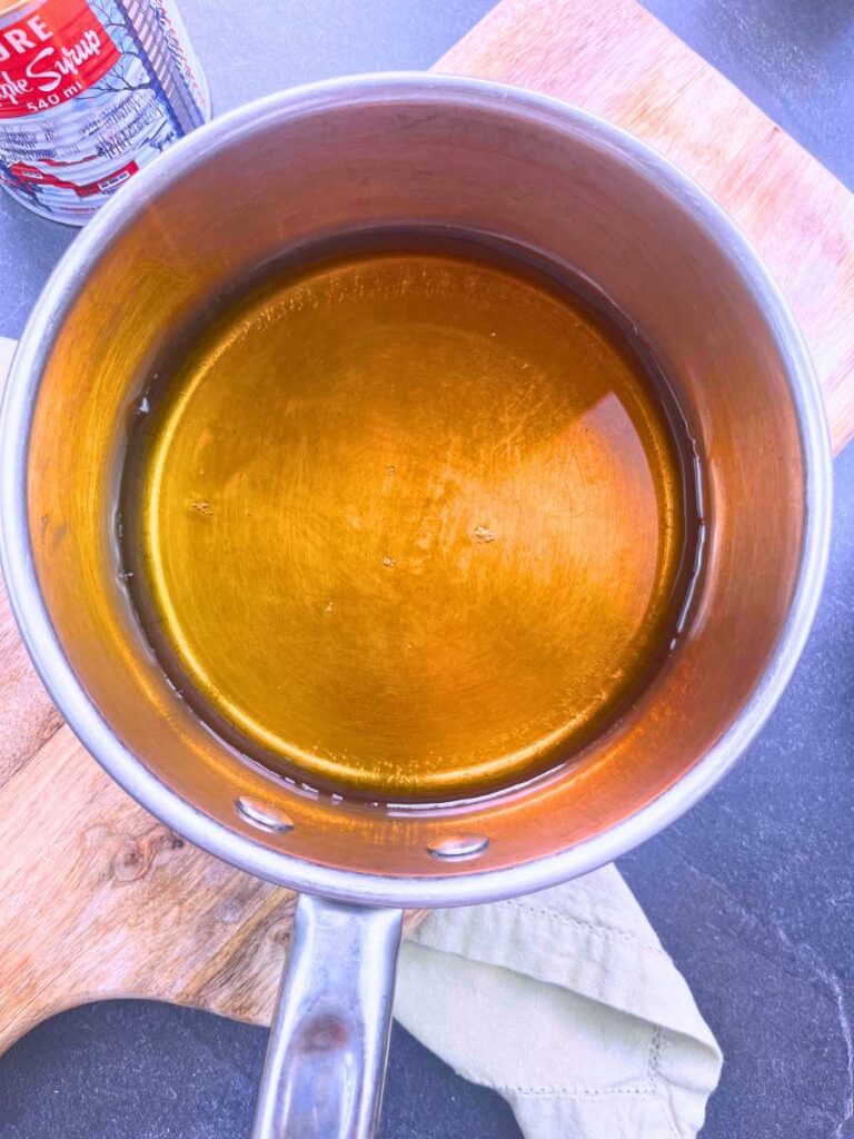 A metal sauce pot with a mixture of maple syrup and water inside.