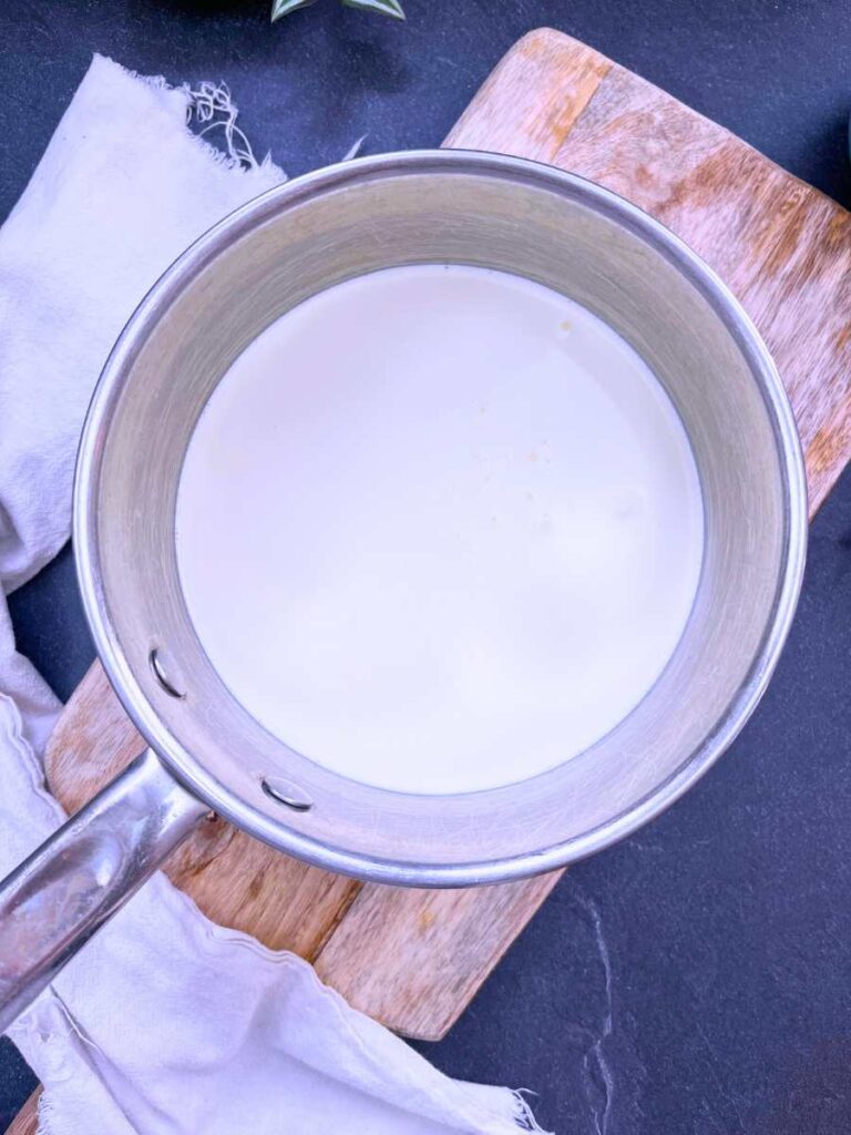 A metal sauce pot with heavy cream inside.