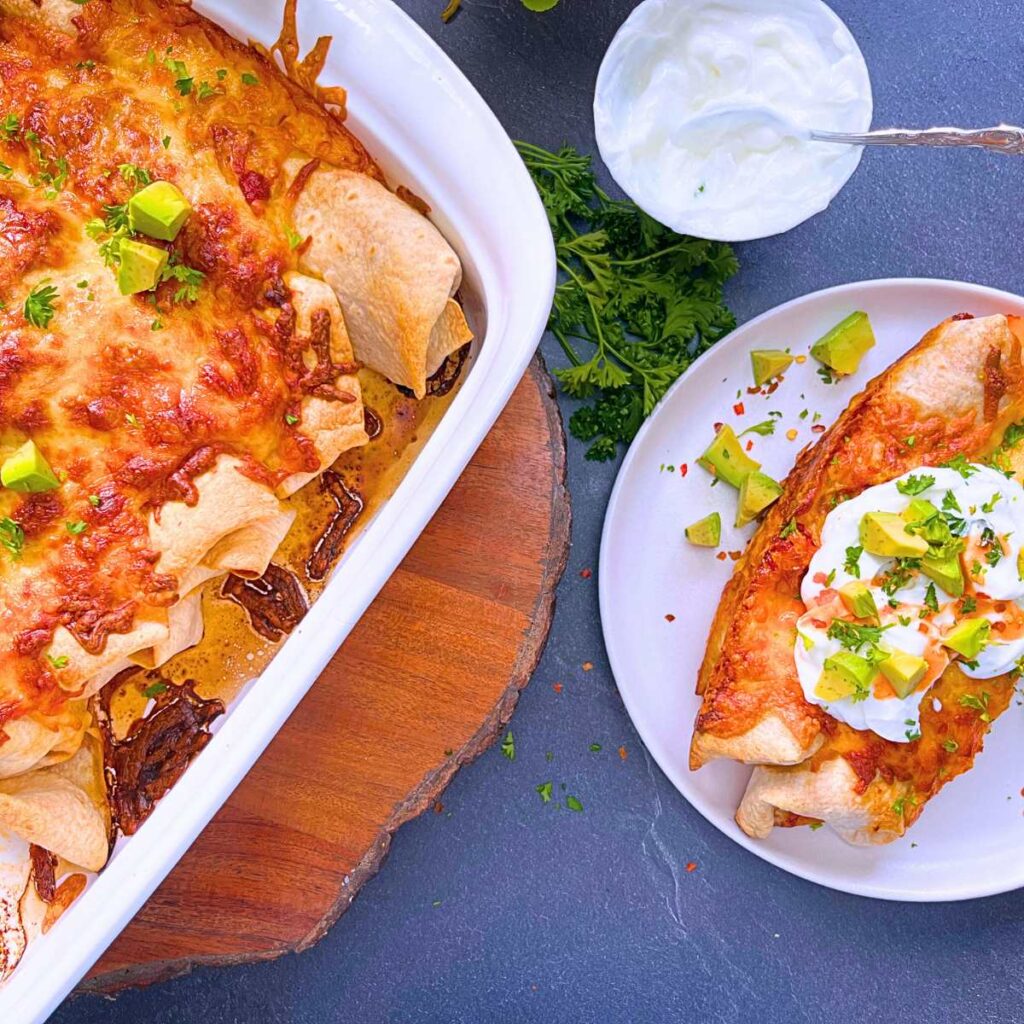 Chicken enchiladas in a white casserole dish. Two have been removed and are on a white plate.