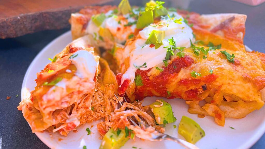 Two chicken enchiladas on a white plate. One has been split in half to show the shredded chicken inside.