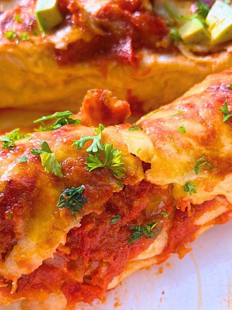 A side view of a chicken enchilada in a white casserole dish. There are more in the background.