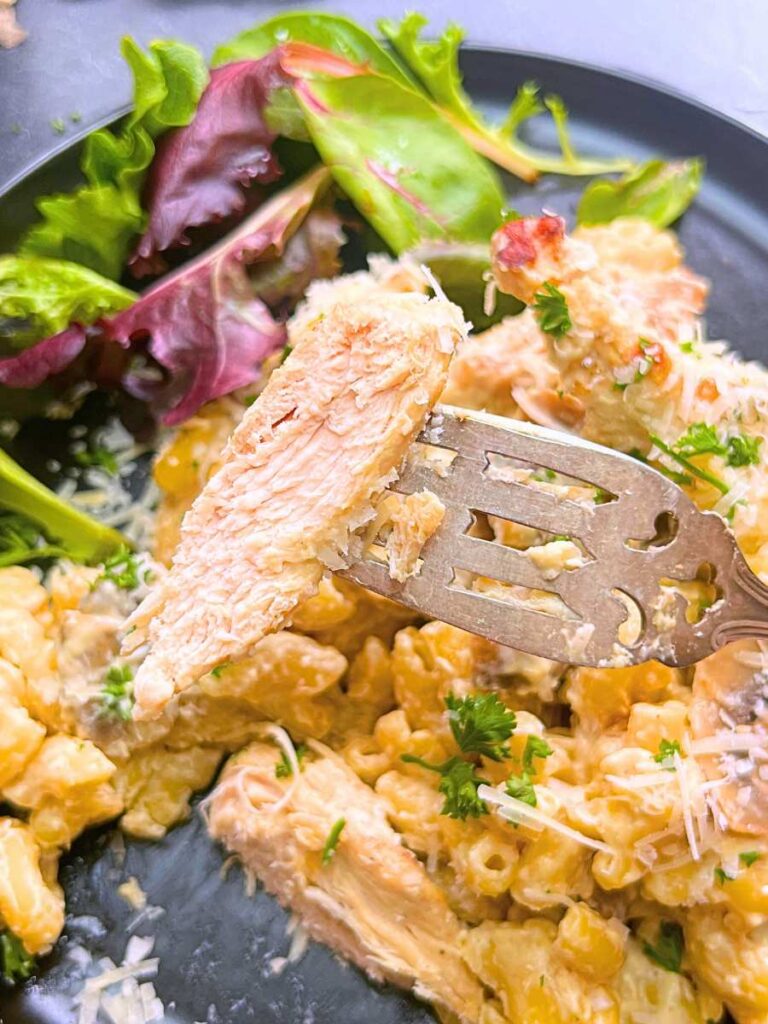 A black plate with a chicken stroganoff pasta. There is a woman holding a piece of the chicken on a fork.