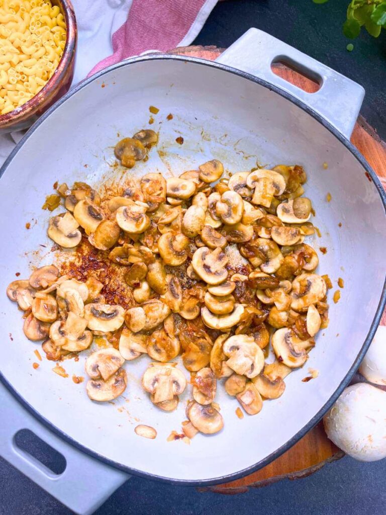 Mushrooms, garlic, and onions frying in a grey Dutch oven.