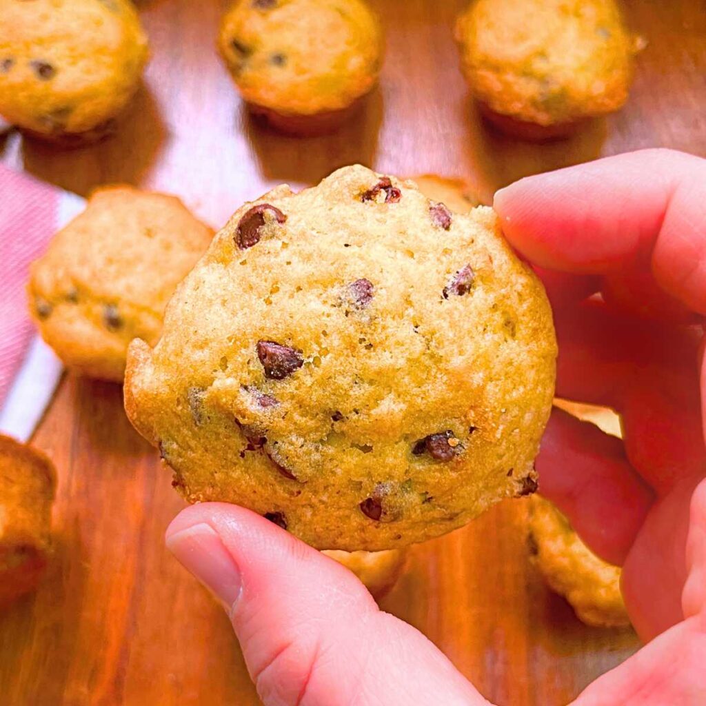 A woman is holding a mini banana chocolate chip muffins.