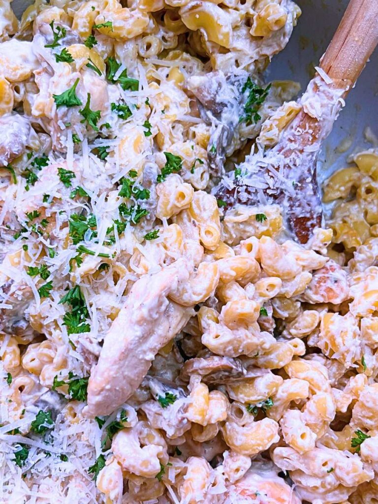 A pot of chicken stroganoff pasta. There is a wooden spoon inside.