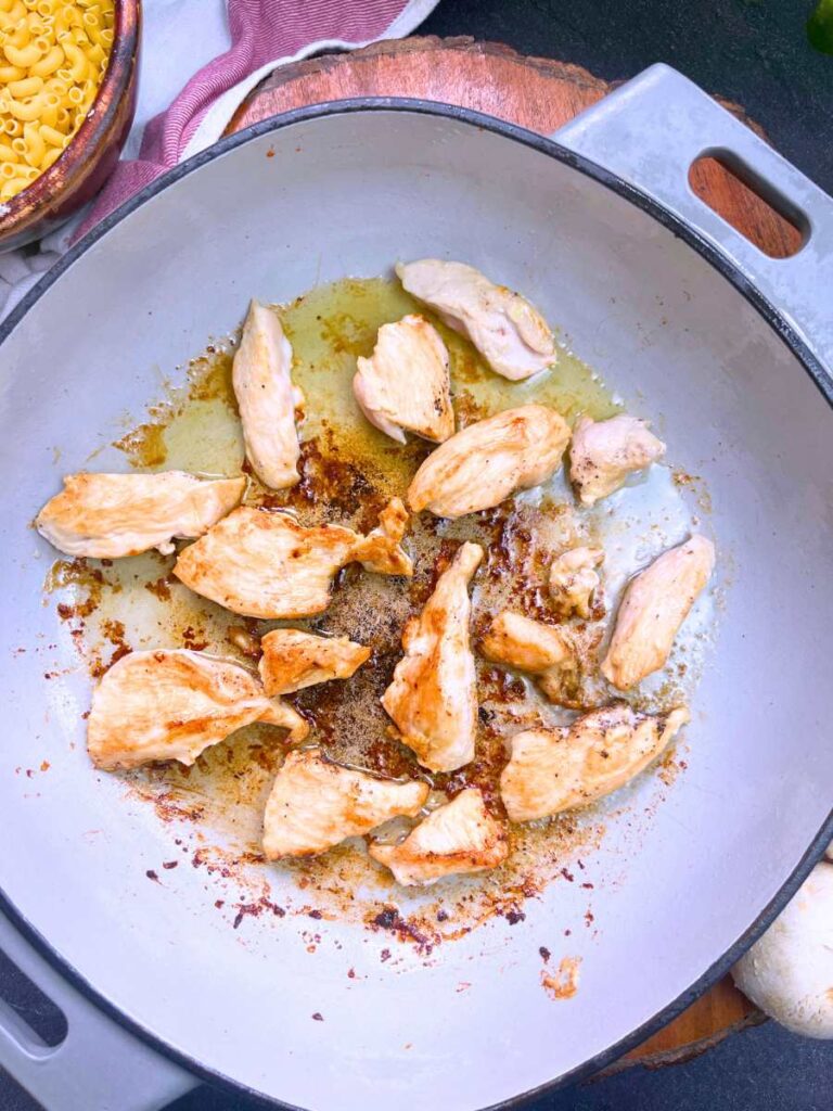 Strips of chicken frying in a grey pan.