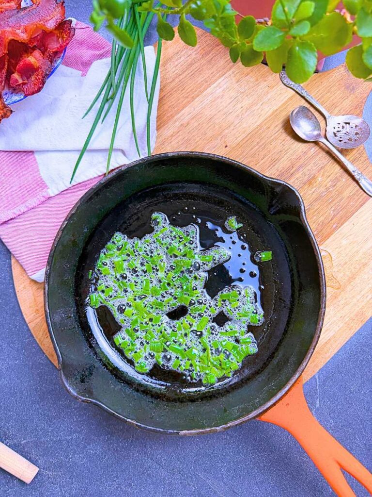 A pan with bacon grease and diced chives inside.
