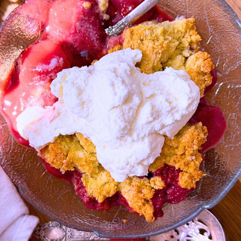 A serving of a baked strawberry cobbler with whipped cream on top.