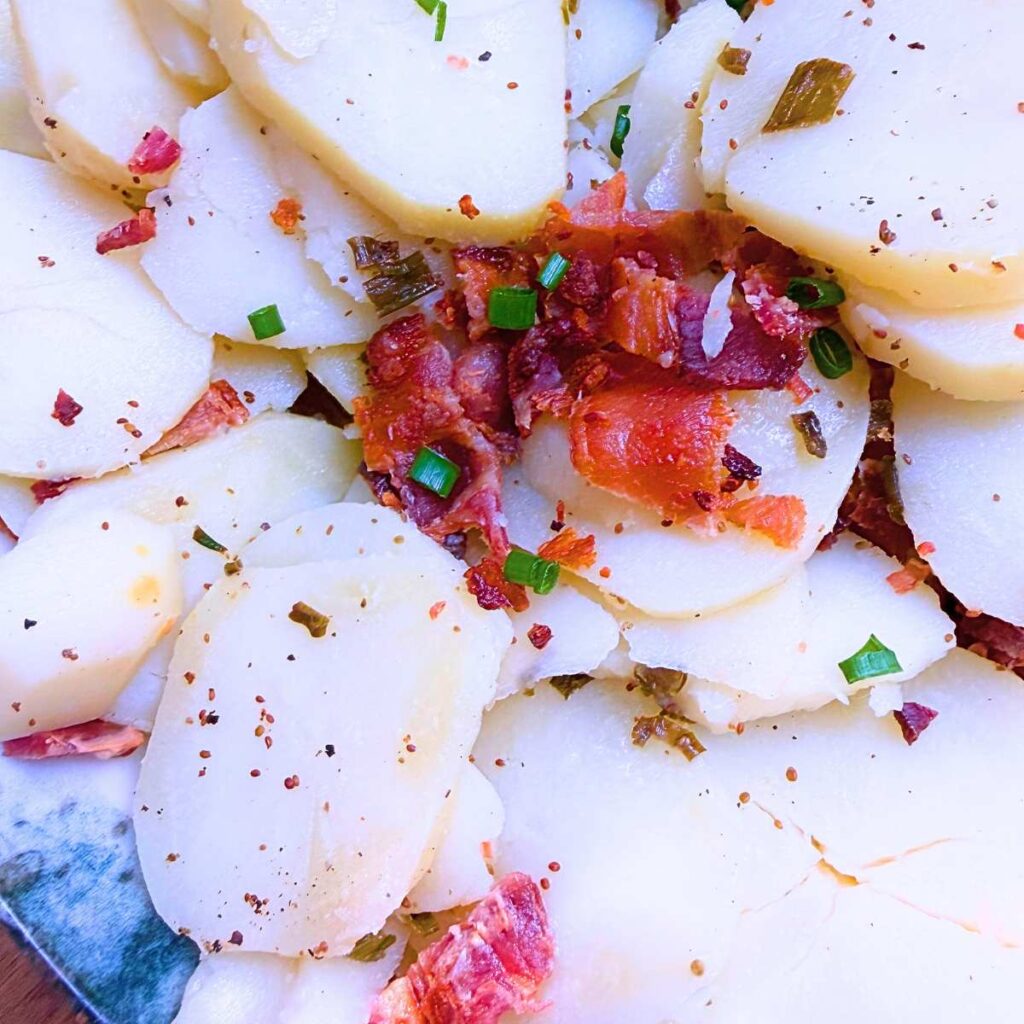 A close up look at a sliced potato salad without mayonnaise. There is bacon and chives on top.