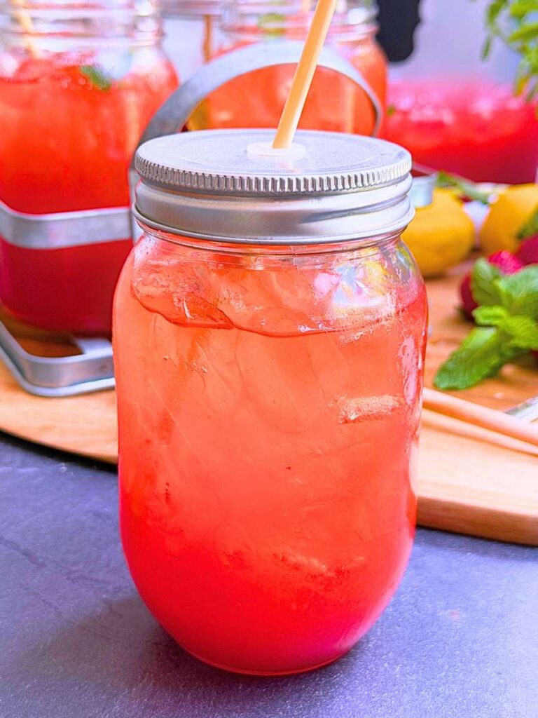 A canning jar glass of strawberry iced tea. There are more in the background.