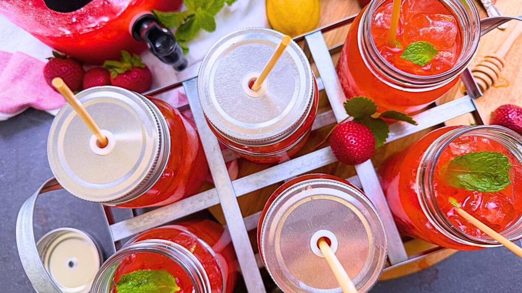 An overhead view of some glasses of strawberry iced tea. Some have lids and straws.