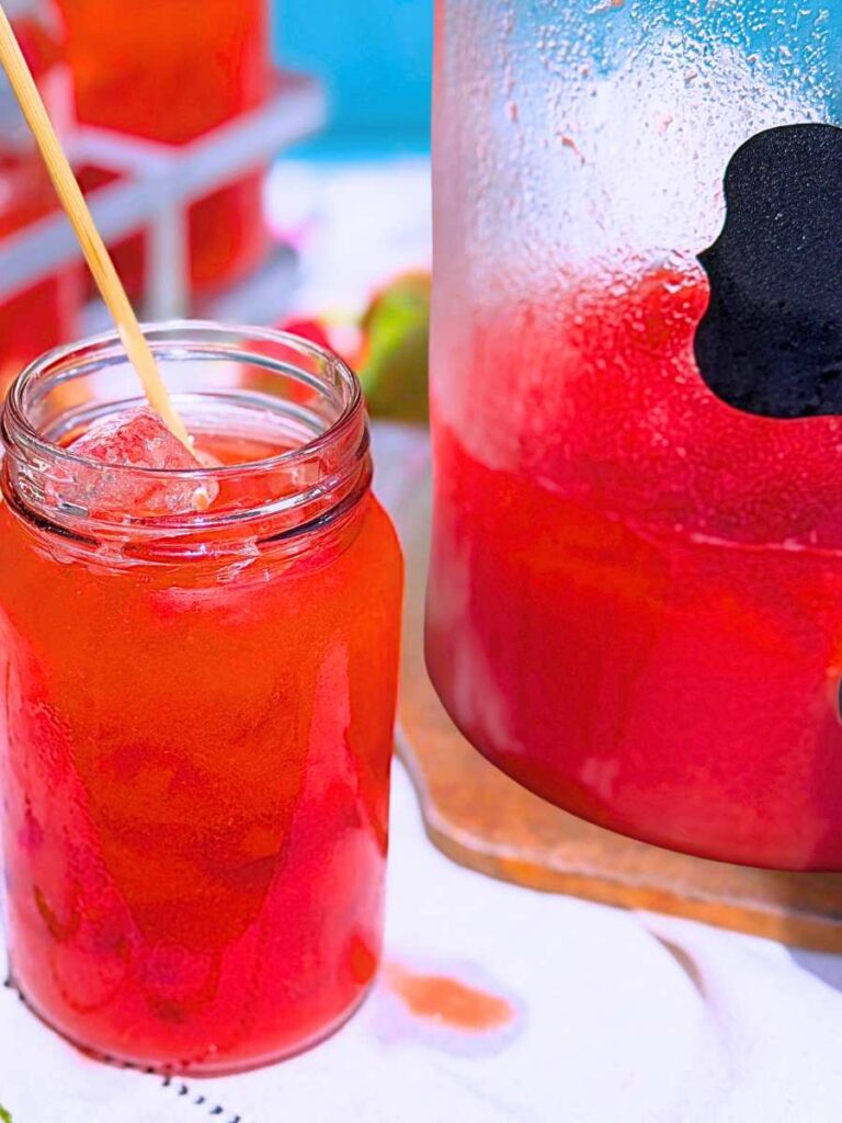 A pitcher of strawberry iced tea. There is a glass filled with iced tea in front.