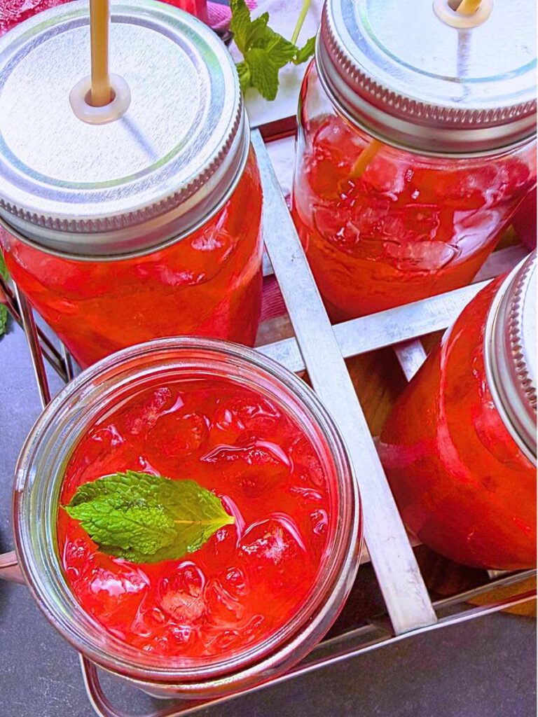 A glass of strawberry iced tea with mint leaves on top. There are more glasses around it.