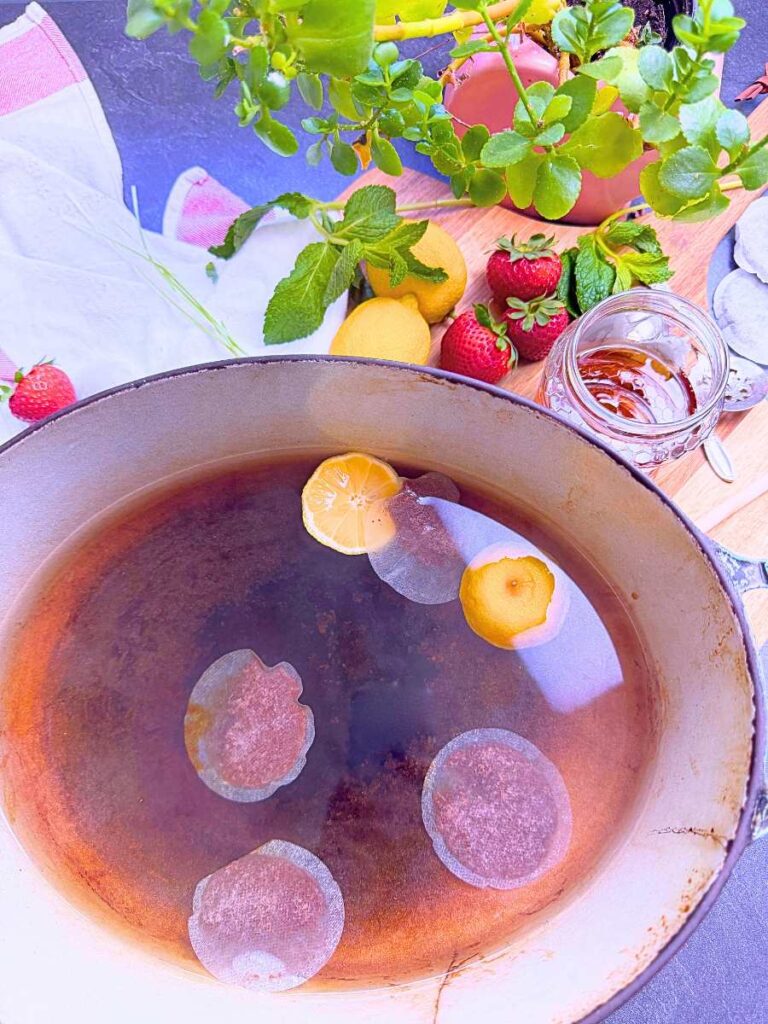 A large pot with tea bags, water, and lemon.