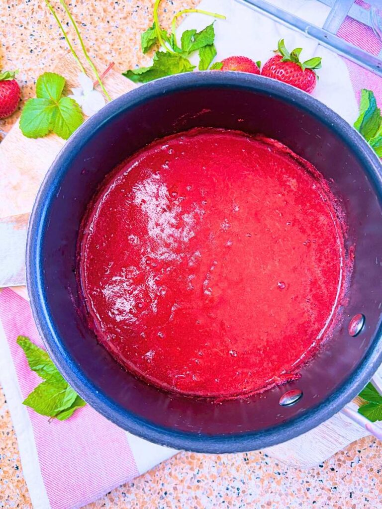A purée of strawberries in a black sauce pot.